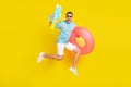 Photo of funky sweet young guy dressed blue t-shirt eyewear jumping holding inflatable rings water gun isolated yellow Royalty Free Stock Photo