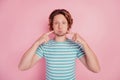 Photo of funny crazy foolish man fingers press cheeks wear casual blue striped t-shirt on pink background