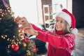 Photo of funny excited small girl wear red print sweater enjoying hanging new year xmas tree baubles indoors house room Royalty Free Stock Photo