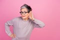 Photo of funny expression mature age woman touch ear listening copyspace hearsay secrets isolated over pastel pink color