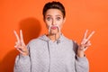 Photo of funny funky young woman dressed grey hoodie showing v-signs having fun isolated orange color background Royalty Free Stock Photo