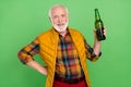 Photo of funny handsome mature man dressed yellow waistcoat smiling holding beer bottle isolated green color background Royalty Free Stock Photo