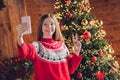 Photo of funny positive cute girl hold telephone make selfie demonstrate v-sign newyear evergreen tree illumination Royalty Free Stock Photo