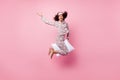 Photo of funny pretty curly dark skin woman dotted nightwear riding white pillow jumping high isolated pink color