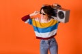 Photo of funny pretty young lady dressed striped pullover arm dark glasses holding boom box isolated orange color Royalty Free Stock Photo