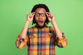 Photo of funny shocked dark skin man wear plaid shirt arms spectacles open mouth green color background