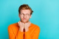 Photo of funny unsure young man wear orange pullover spectacles arms chin looking empty space isolated teal color