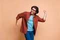 Photo of funny young man dance raise fists cheerful face wear eyeglasses brown t-shirt isolated beige color background