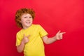 Photo of ginger little boy indicate forefingers empty space wear yellow t-shirt isolated red color background