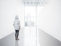 Photo of girl in empty contemporary gallery looking at the blank white canvas. Big windows, spotlights, concrete floor