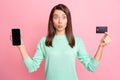 Photo of girl hold phone screen empty space debit card send air kiss wear teal pullover isolated pink color background