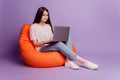 Photo of girl with laptop sit beanbag look screen on purple background