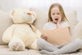 Photo of girl and teddy bear sitting on the sofa with a book in hands. Royalty Free Stock Photo