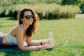 Photo of glad relaxed brunette woman poses on fitness mat wears trendy sunglasses and sportswear drinks water as feels thirsty