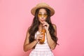 Photo of glamour woman 20s wearing sunglasses and straw hat drinking juice from glass bottle, isolated over pink background Royalty Free Stock Photo