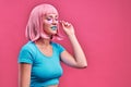 Photo of glamour young woman with blue lips wearing pink wig touching sunglasses and looking aside isolated over pink background Royalty Free Stock Photo