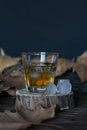 A glass of whiskey with ice, stands on a wooden stand with melting ice cubes on a background of autumn leaves, on the table