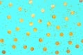 Photo of gold confetti sprinkles in different sizes on pastel cyan backdrop. Christmas pattern. Festive holiday