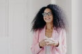 Photo of good looking African American prosperous busineswoman waits for partner in office, drinks coffee discusses future plans