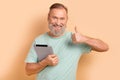 Photo of good mood person dressed teal t-shirt holding tablet showing thumb up approve good work isolated on beige color Royalty Free Stock Photo