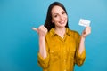 Photo of good mood pretty girl dressed yellow shirt rising credit card thumb empty space isolated blue color background