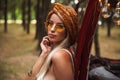 Photo of gorgeous hippy woman, wearing stylish accessories looking forward while resting in forest camp Royalty Free Stock Photo