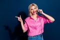 Photo of gorgeous woman with bob hair dressed pink shirt in headset indicating at discount empty space isolated on dark Royalty Free Stock Photo