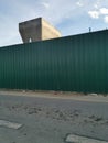 Photo of green zinc fence on asphalt road and partially concrete pillar in the morning Royalty Free Stock Photo