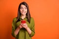 Photo of guilty young girl hold smartphone bite lip look side empty space wear green shirt isolated orange color