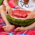 Half of a ripe huge watermelon, which is hugged by the hands and feet of a little girl. Juicy ripe fruit. Summertime. Harvest.
