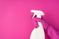 Photo of hand in pink rubber glove holding detergent spray bottle without label pressing atomizer on isolated pink background with Royalty Free Stock Photo