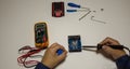 Photo of the hands of a man using a soldering iron to repair a battery pack electrical board. Homemade repair work