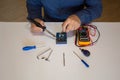 Photo of the hands of a man using a soldering iron to repair a battery pack electrical board. Homemade repair work