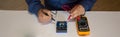 Photo of the hands of a man using a tester to repair an electrical board of a battery pack. Horizontal banner