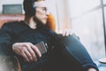 Photo handsome bearded man headphones listening to music modern loft studio.Man sitting in vintage chair looking window,holding sm