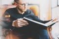 Photo handsome bearded scientist wearing glasses black shirt.Man sitting in vintage chair university library, reading book and rel