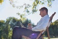 Portrait of handsome businessman drinking coffee and reading newspaper while sitting on folding chair in park Royalty Free Stock Photo