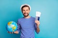 Photo of handsome cheerful guy hold world globe addicted traveler show tickets wait flight check-in wear striped sailor