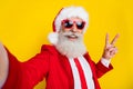 Photo of handsome cool santa dressed red suit tie showing v-sign recording video vlog isolated yellow color background Royalty Free Stock Photo