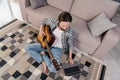Photo of handsome funny young man wear plaid shirt smiling sitting floor playing guitar typing modern gadget indoors Royalty Free Stock Photo