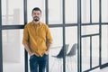 Photo of handsome guy holding hands in pockets standing in modern stylish interior apartments indoors near conference