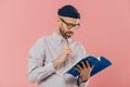 Photo of handsome male author has dark bristle, holds pencil and book, underlines necessary information, over pink studio