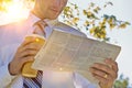 Portrait of handsome mature businessman holding cup of coffee while reading newspaper in park during break Royalty Free Stock Photo