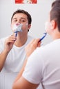 Photo of handsome young man shaving and looking at himself in th Royalty Free Stock Photo