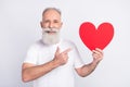 Photo of happy charming attractive old man point finger large red paper heart isolated on grey color background