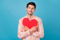 Photo of happy charming young positive man hug heart shape red paper smile isolated on blue color background Royalty Free Stock Photo