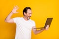 Photo of happy cheerful mature man look hold laptop wave hello webcamera isolated on yellow color background Royalty Free Stock Photo