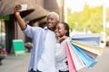 Photo of happy couple. Cheerful african american man makes selfie, girlfriend with bags hugs guy