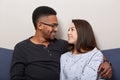 Photo of happy couple in love look smiling at each other, being at home, spending time together, watch films while sitting on sofa