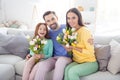 Photo of happy family hug cuddle enjoy time together positive smile girls hold flowers bouquet spring sit couch home